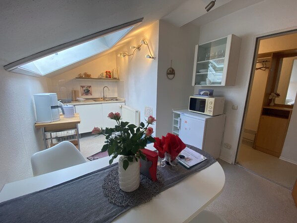 Een compacte keuken met dakraam, een zithoek met tafel en stoelen, en een kleine koelkast.