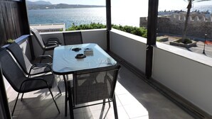 Un balcón con mesa y sillas, que da a una masa de agua y un paisaje urbano costero.