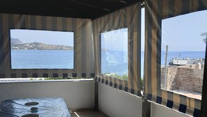 Un porche cubierto con mesa y sillas, amplias ventanas con vistas al mar y acantilados.