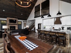 A spacious kitchen with a large island, wooden flooring, and a stone fireplace.