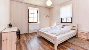 Un dormitorio con cama de madera, un radiador, una ventana y una lámpara colgante.