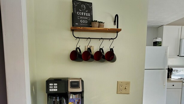 Una kitchenette con una cafetera, tazas y un letrero en la pared.