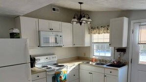 Una cocina compacta con armarios blancos, estufa, microondas y refrigerador.