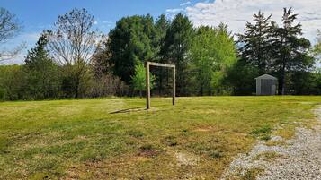 A grassy field with a wooden structure, a gravel path, and a shed in the background.