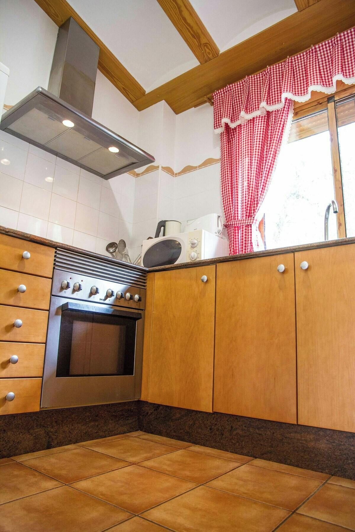 A kitchen with wooden cabinets, a stainless steel stove, and a red and white checkered curtain.