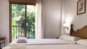 Une chambre d’hôtel avec deux lits, un balcon donnant sur un espace verdoyant, une lampe et un tableau au mur.