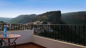 Un balcon avec une table et des chaises, donnant sur une ville avec ses bâtiments et un imposant promontoire rocheux.