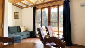 Une pièce avec un plafond en bois, un canapé, deux fauteuils, une table et de grandes fenêtres avec des rideaux.