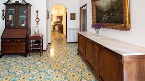 A hallway with patterned floor tiles, a wooden cabinet, a clock, and a framed painting on the wall. - Apartment Bianca with shared pool (Sorrento)