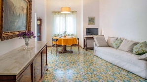 A living room with a patterned floor, a sofa, a dining table with chairs, a TV, and a painting on the wall. - Apartment Bianca with shared pool (Sorrento)