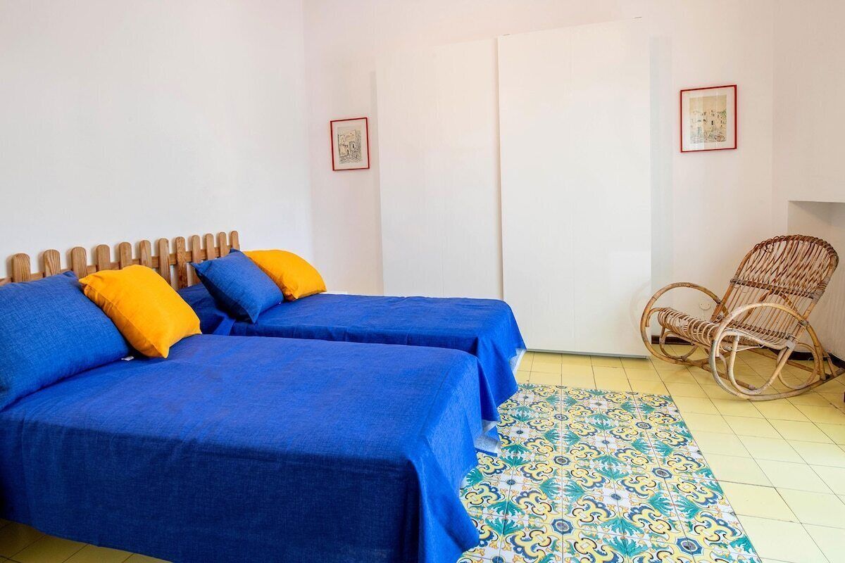 Une chambre avec deux lits recouverts de draps bleus, une chaise en osier et un tapis à motifs.
