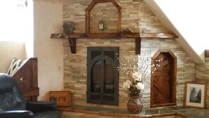 Una sala de estar acogedora con una chimenea de piedra, un sofá de cuero negro y un banco de madera.