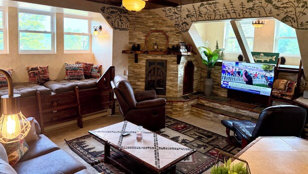 Una sala de estar acogedora con chimenea, asientos cómodos, televisión y ventilador de techo.