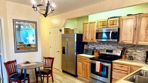 Una cocina moderna con armarios de madera, electrodomésticos de acero inoxidable, un comedor con dos sillas y una araña.