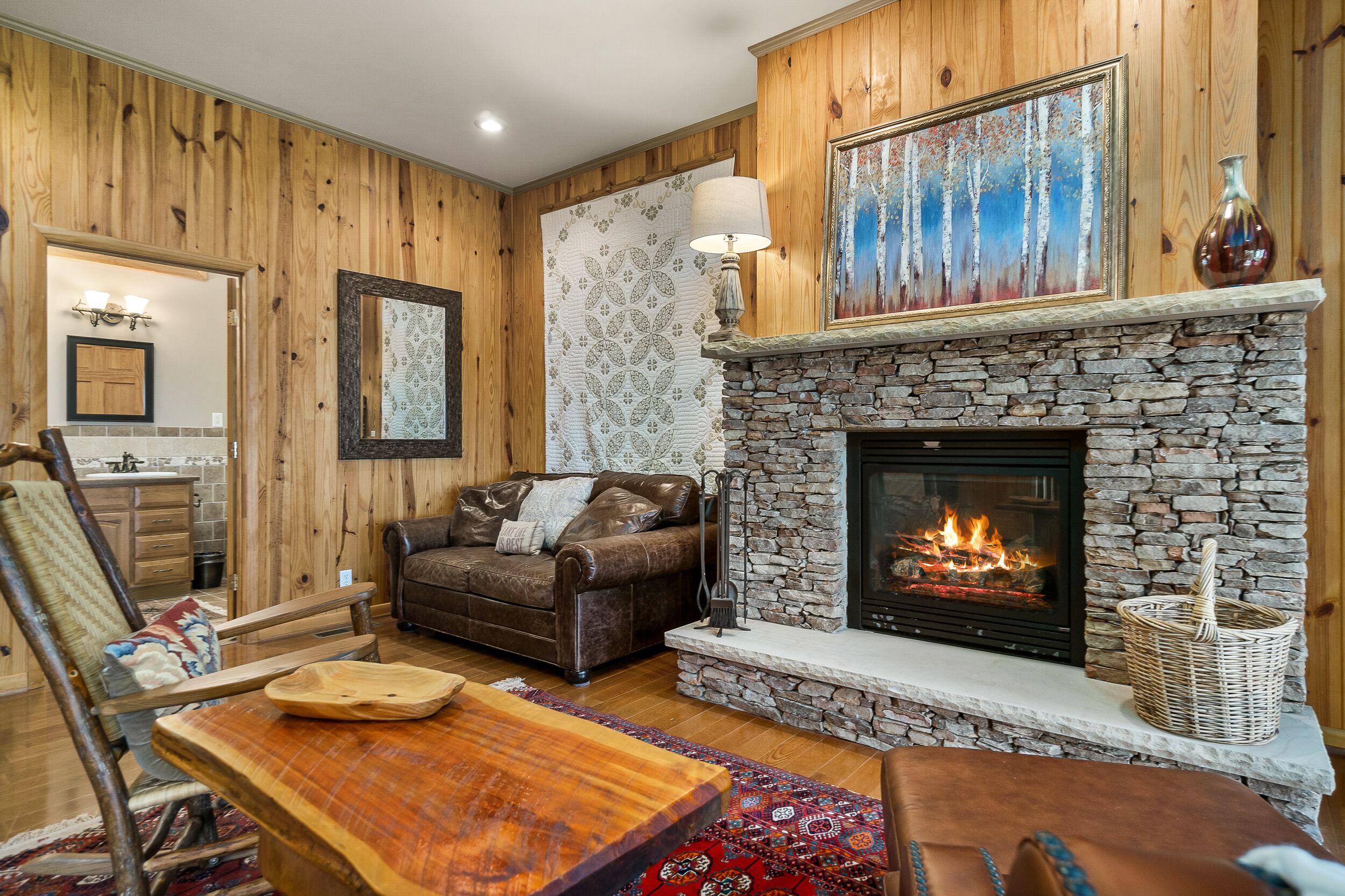 Ein gemütliches Wohnzimmer mit Kamin aus Stein, Holzwänden, einem braunen Ledersofa und einem Esstisch.
