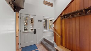 Un escalier en bois avec une rampe, une porte blanche avec une fenêtre et un paillasson bleu à l’entrée.