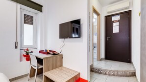 Ett litet, rent rum med ett skrivbord i trä, en stol, en tv som är monterad på väggen och en dörr med en skylt.