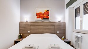 Ett hotellrum med en sänggavel i trä, en inramad tavla, sänglampor, ett element och prydligt hopvikta handdukar på sängen.