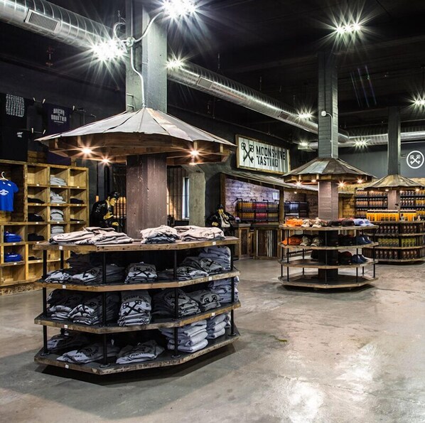 A spacious indoor market with high ceilings and exposed ductwork. Shelves are stocked with various items, and a sign for 'Moonshine Tasting' is visible.