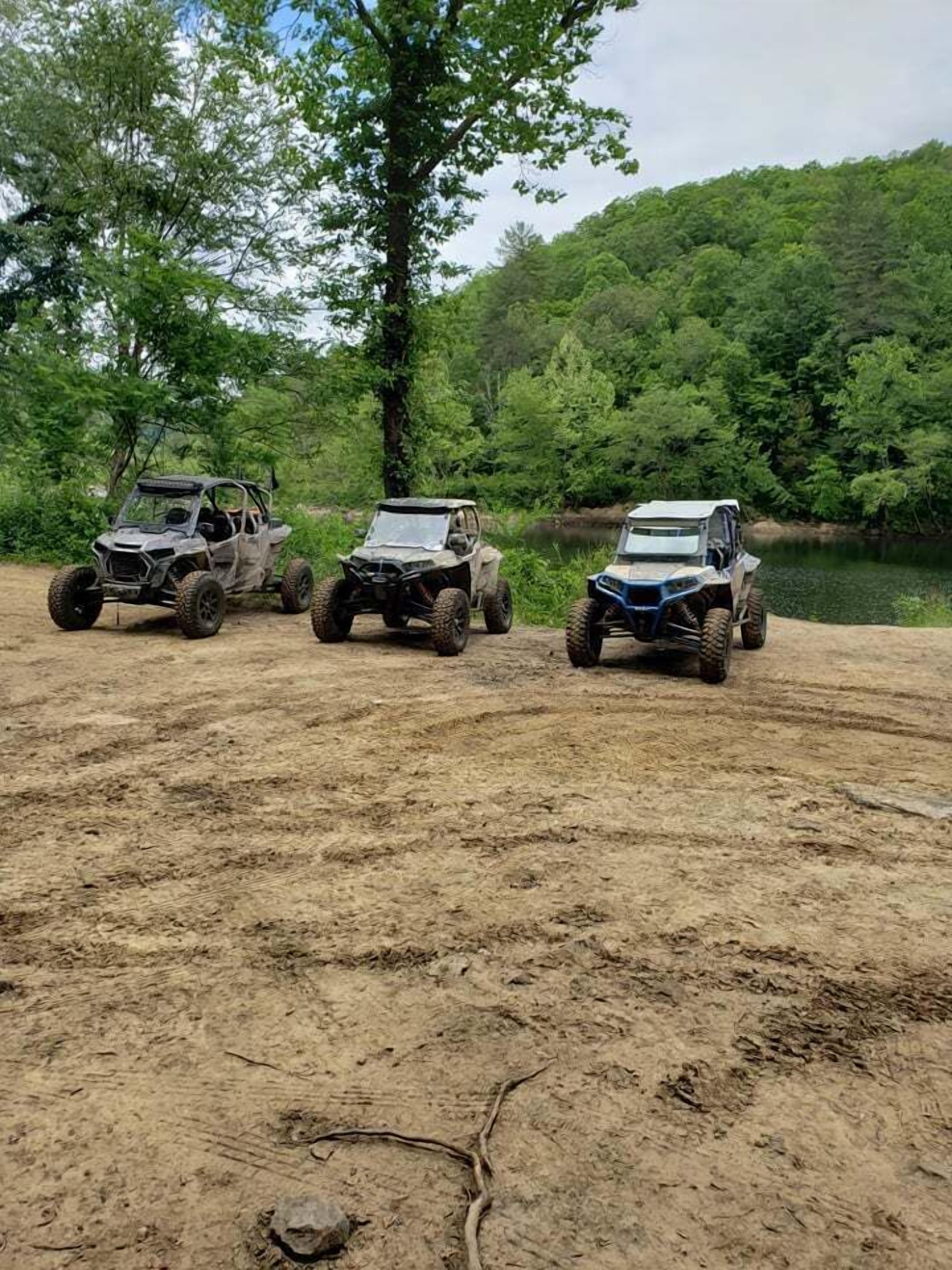 Three off-road vehicles parked on a dirt path with a forested area in the background.