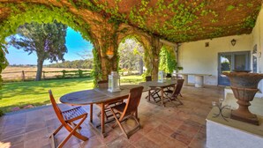 An outdoor patio with wooden furniture, a large urn, and a view of a grassy field. - Casale Teresa (Tarquinia)