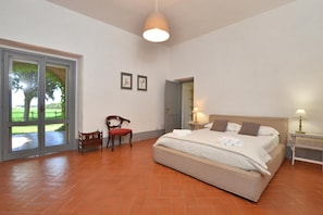 A bedroom with a bed, a chair, a nightstand, a lamp, a door, and a window.