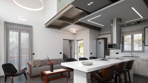 Una cuina moderna amb una illa central, electrodomèstics integrats i zona de menjador amb sofà i cadires.