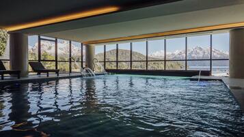 Una piscina interior con vistas despejadas a montañas a través de amplias ventanas.