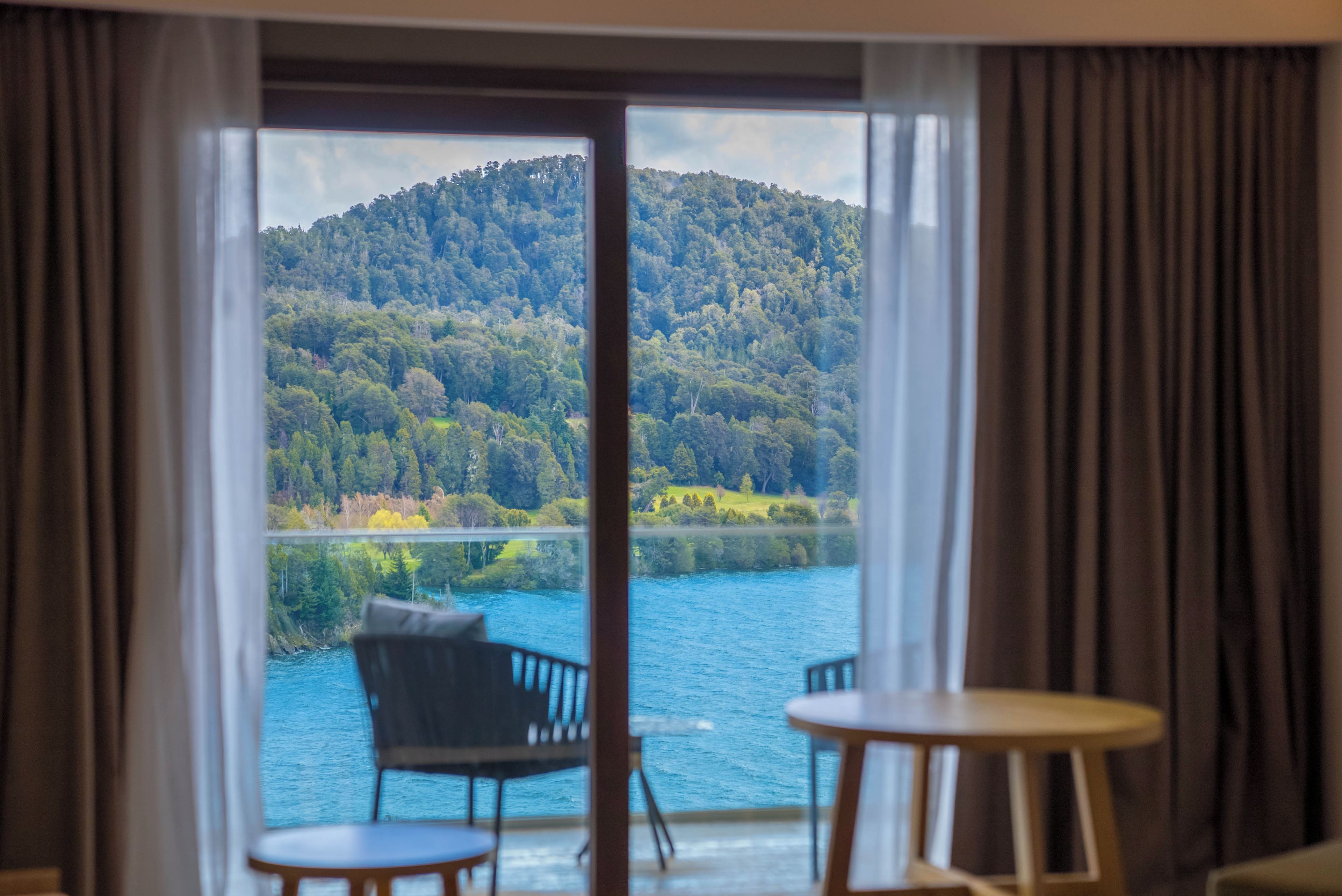 Une pièce avec vue sur un lac et une forêt. On aperçoit un fauteuil et une table au premier plan.