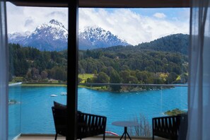 Una habitación con vista a un lago y montañas. Hay dos sillas y una pequeña mesa.