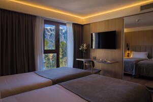 A hotel room with two beds, a desk, a flat-screen TV, and a window with curtains.
