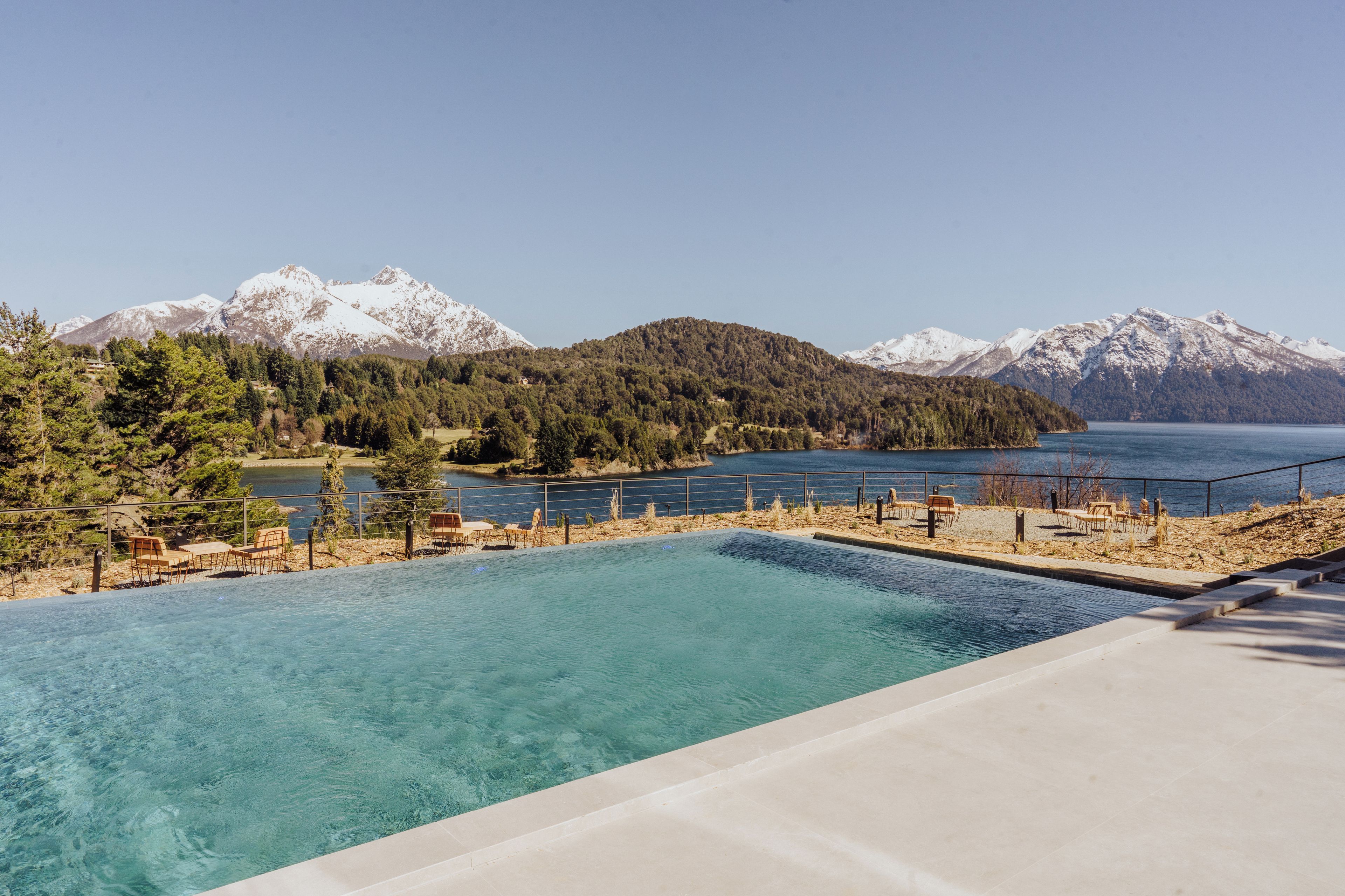 Une piscine d’eau cristalline, d’un bleu éclatant, avec une vue sur un lac et des montagnes en arrière-plan.