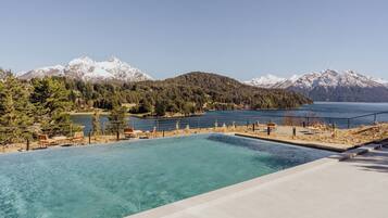 Une piscine d’eau cristalline, d’un bleu éclatant, avec une vue sur un lac et des montagnes en arrière-plan.