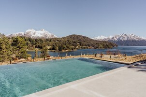 Una piscina azul cristalina con vistas a un lago y montañas al fondo.