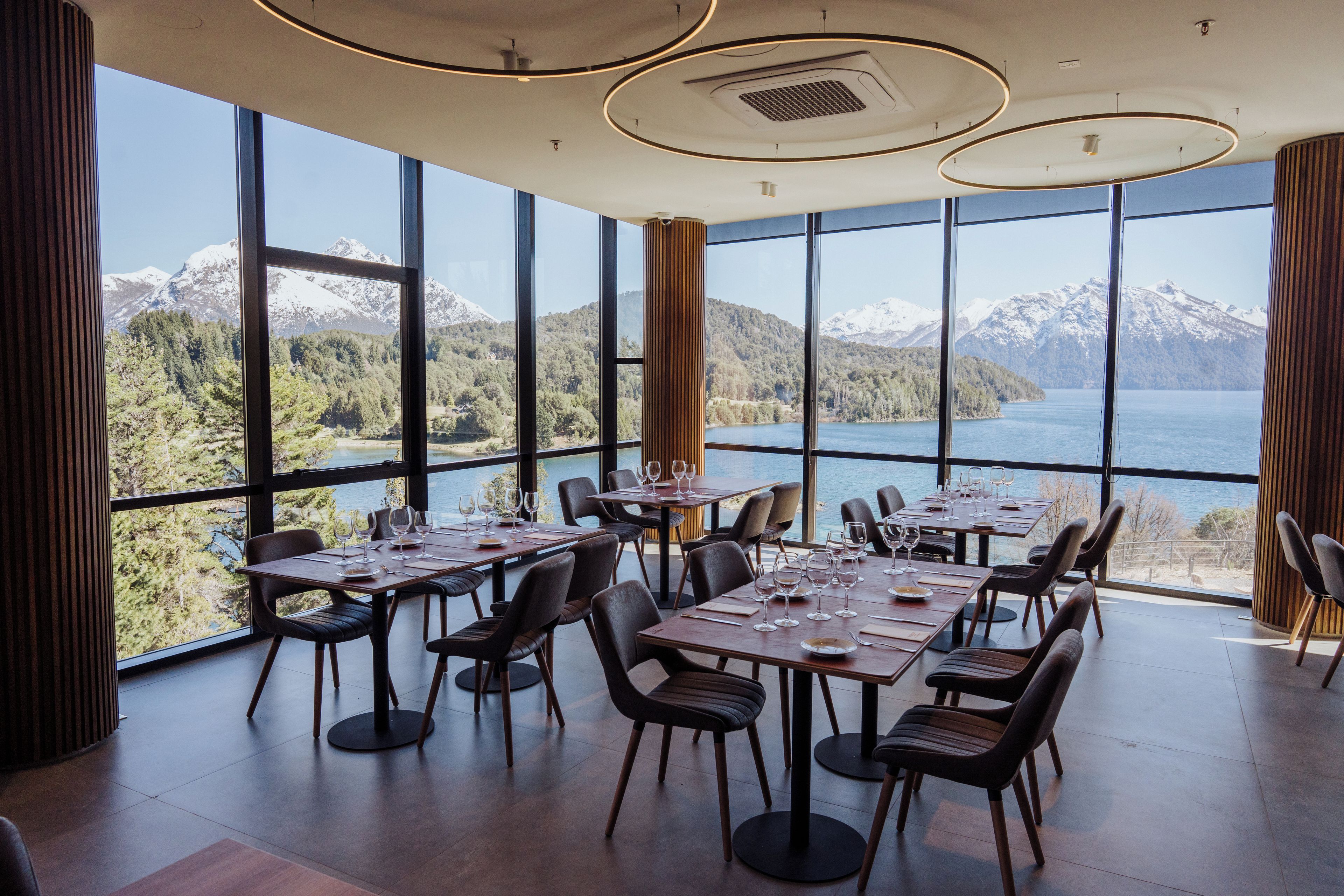 Une salle à manger avec des tables dressées pour les convives, de grandes fenêtres offrant une vue sur les montagnes et un lac.