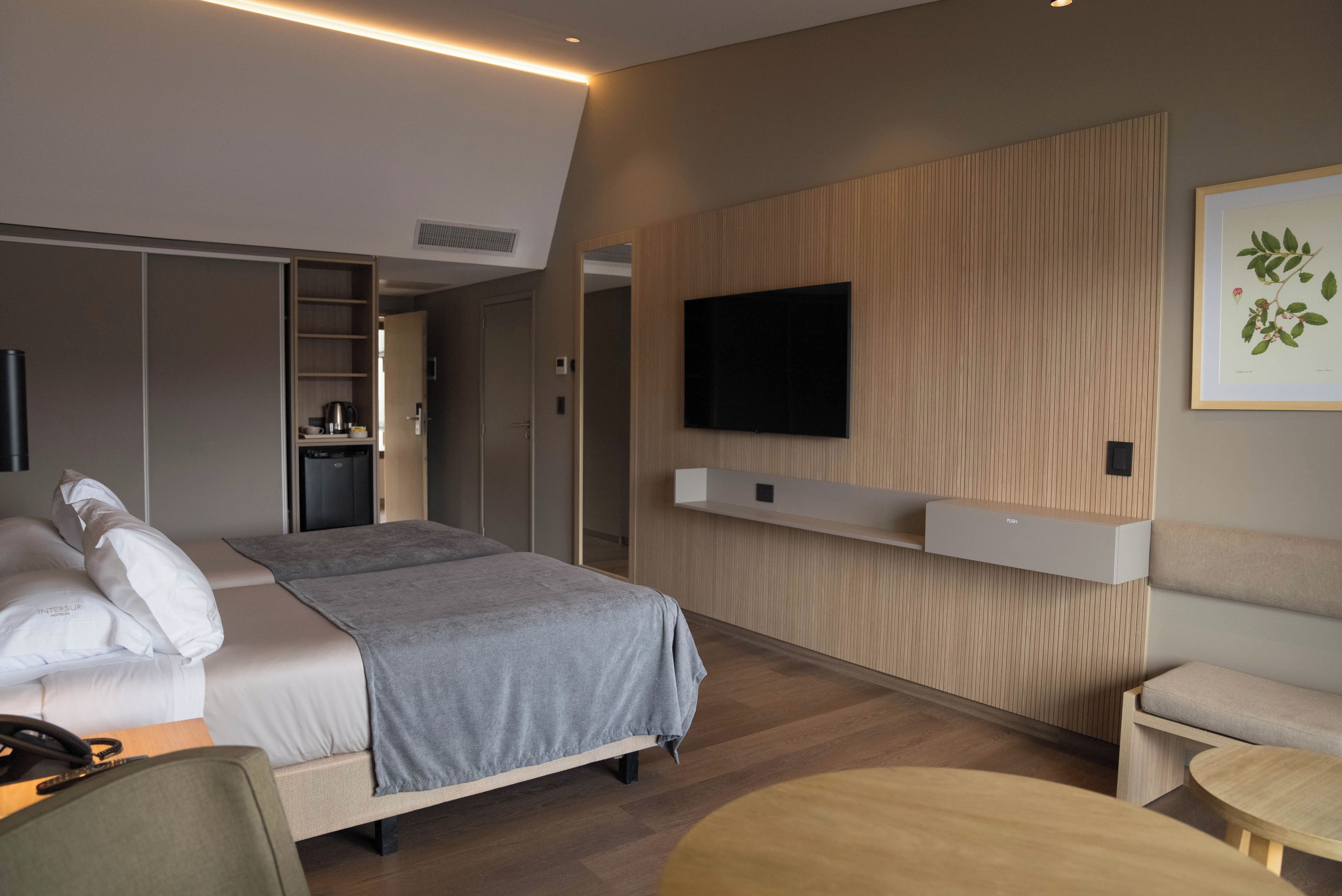 A modern hotel room with a bed, bedside table, and a mounted flat-screen TV.