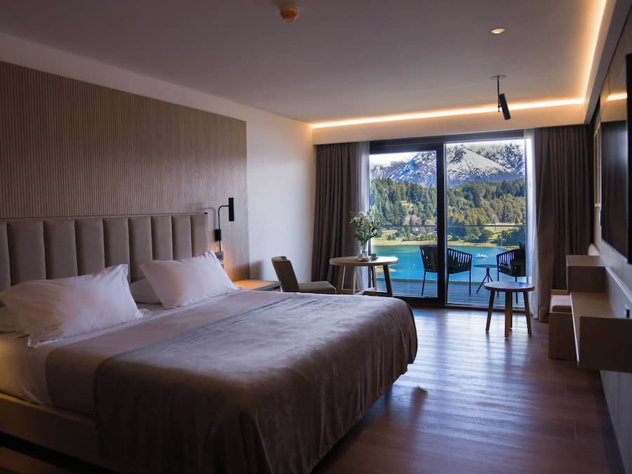 A modern hotel room with a large bed, a seating area with a table and chairs, and a balcony with a scenic mountain view.