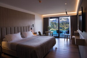 Habitación de hotel moderna con una cama grande, un área de descanso con mesa y sillas, y un balcón con vistas panorámicas a la montaña.