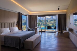 Une chambre d’hôtel moderne dotée d’un grand lit, d’un coin salon avec une table et d’un balcon offrant une vue sur la montagne.