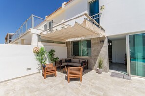Un espace extérieur moderne aménagé avec un canapé et des fauteuils, une terrasse couverte et des plantes en pot.