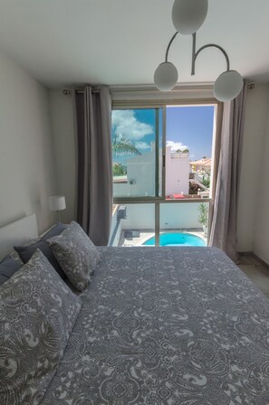Une chambre avec un grand lit, une vue sur une piscine et un balcon avec des rideaux.