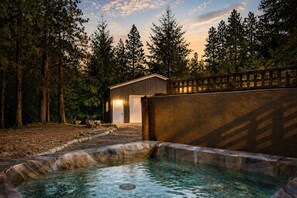 A swimming pool with a stone edge, a wooden deck, and a building with a garage door. - Retro | Hot Tub | Dogs OK | Community Beach | BBQ (Leavenworth)