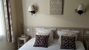 Un letto ben rifatto con lenzuola bianche, due cuscini decorati e asciugamani arrotolati su un copripiumino rosso.