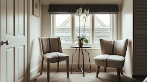 A corner room with two chairs, a small table with a plant, and a window with a view of buildings. - The Falcon Painswick (Stroud)