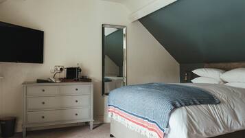 A bedroom with a bed, a dresser, a mirror, and a ceiling with a sloped design.