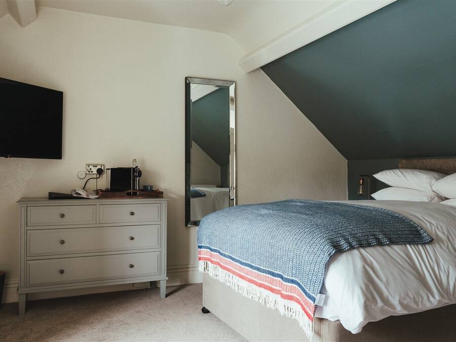 A bedroom with a bed, a dresser, a mirror, and a ceiling with a sloped design.
