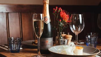 A bottle of Balfour champagne, two glasses, a bowl of food, and a decorative flower arrangement on a wooden table.