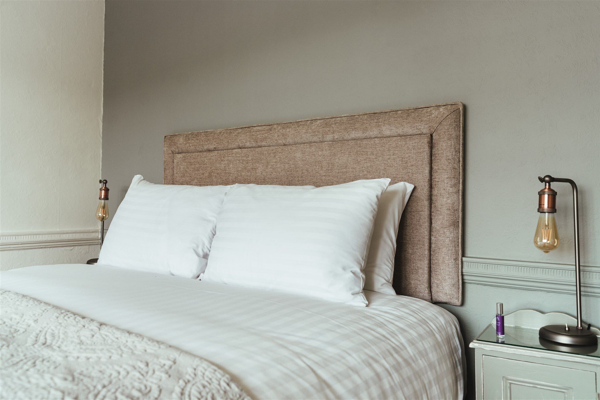 Un lit bien fait, avec une tête de lit à motifs, une table de chevet avec une lampe et un luminaire fixé au mur.