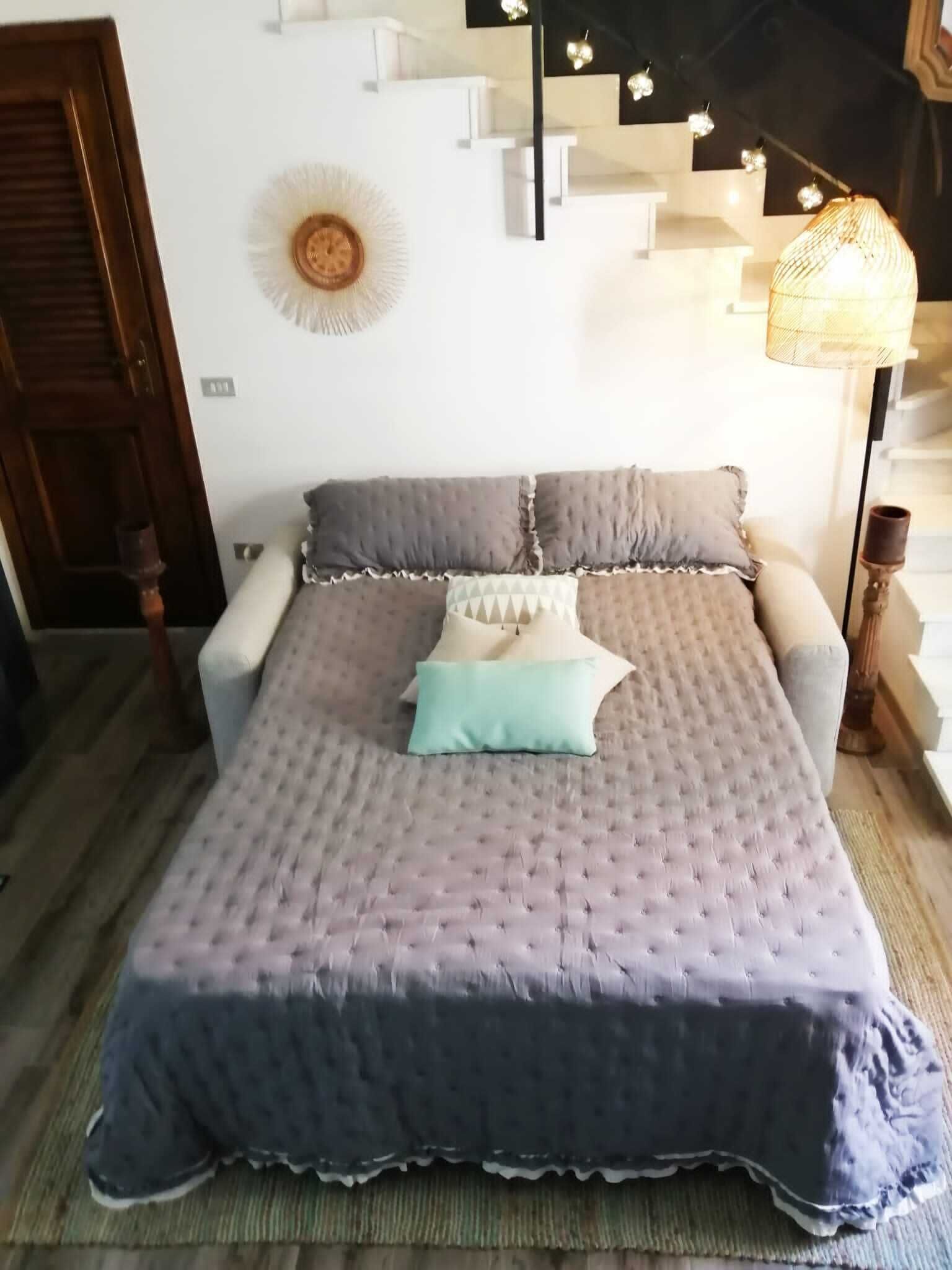 Een net opgemaakt bed met een gebharde sprei, kussens en een decoratieve wandhanger.