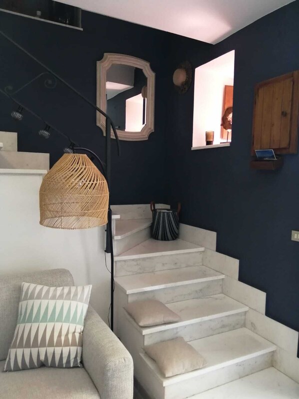 A staircase with white steps, a woven light fixture, a mirror, and a wooden cabinet.